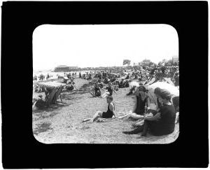 Scene of a beach. 有很多人坐在伞下，在水里玩耍. 图像是黑白的
